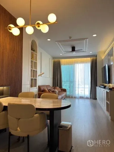 Condominium for rent in Bang Rak, Bangkok - Open-plan living and dining room with round table, pendant light, built-in shelves, sofa, TV wall and balcony.