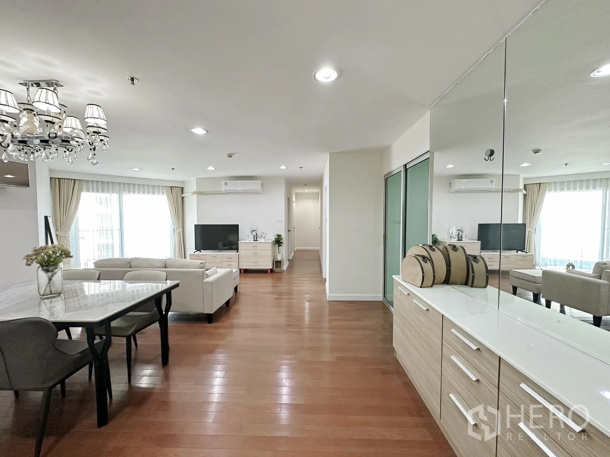 คอนโด for sale in Huai Khwang, Bangkok - มุมมองอีกด้านของพื้นที่นั่งเล่นพร้อมตู้บานกระจก โต๊ะทานอาหาร โซฟา และแสงธรรมชาติ.