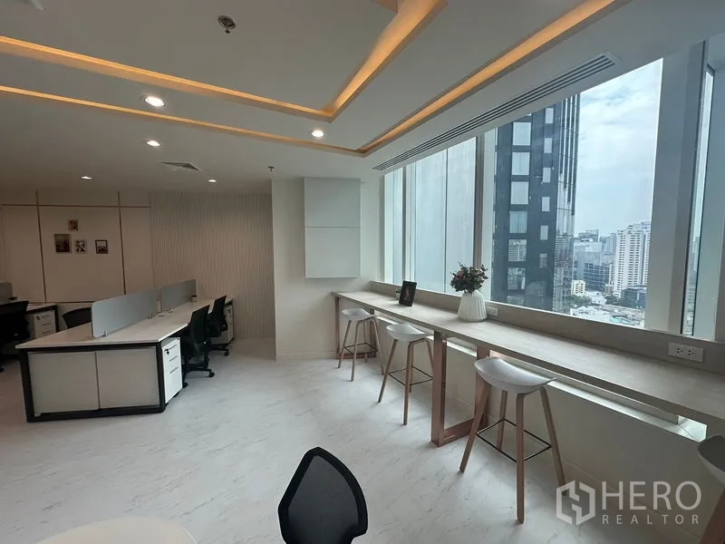 Office Space for rent - High‑rise Sukhumvit skyline seen from long window counter with stools.