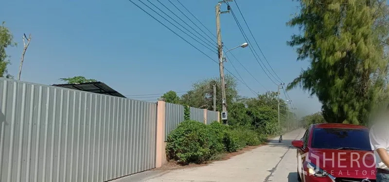 คลังสินค้า ให้เช่าในKhlong Sam Wa, Bangkok - รั้วเมทัลชีทและสายไฟฟ้าตามแนวถนนทางเข้าโกดัง มีรถยนต์จอดริมทาง