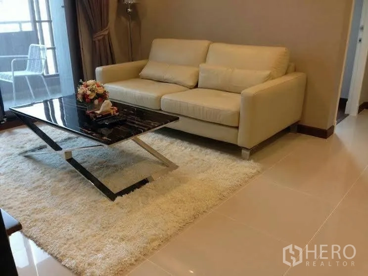Condominium for rent or sale in Huai Khwang, Bangkok - Close-up of beige sofa with pillows and a black marble coffee table on a plush rug beside the balcony doors.
