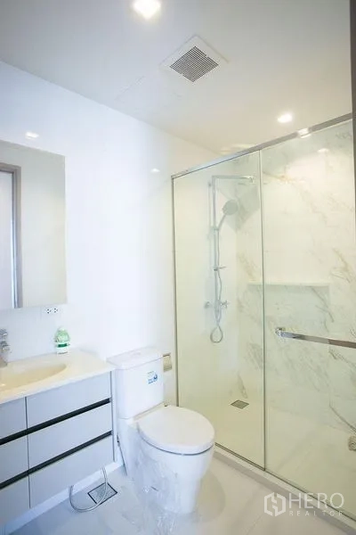 公寓 出租在Watthana, Bangkok - 明亮浴室，玻璃淋浴间、坐便和白色盥洗台。