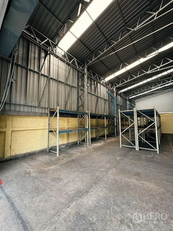 Warehouse for rent in Din Daeng, Bangkok - Interior of the warehouse with high steel-truss ceiling, skylights, concrete floor and storage racks.