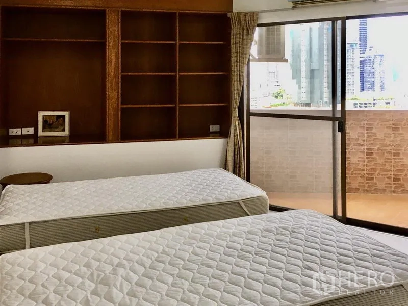 Condominium for rent in Watthana, Bangkok - Secondary bedroom with twin beds, built-in shelves and sliding glass door to a balcony with city views.