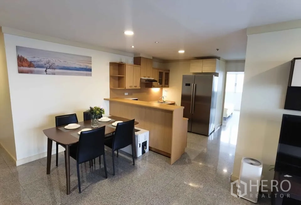 Condominium for rent in Khlong Toei, Bangkok - Dining table beside open kitchen with wooden cabinets and double-door fridge.