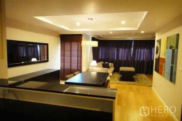 Condominium for rent in Sathon, Bangkok - Open-plan living and dining area with recessed lights, wood floors, dark curtains and a modern dining table viewed from the kitchen counter in a Sathorn condo.