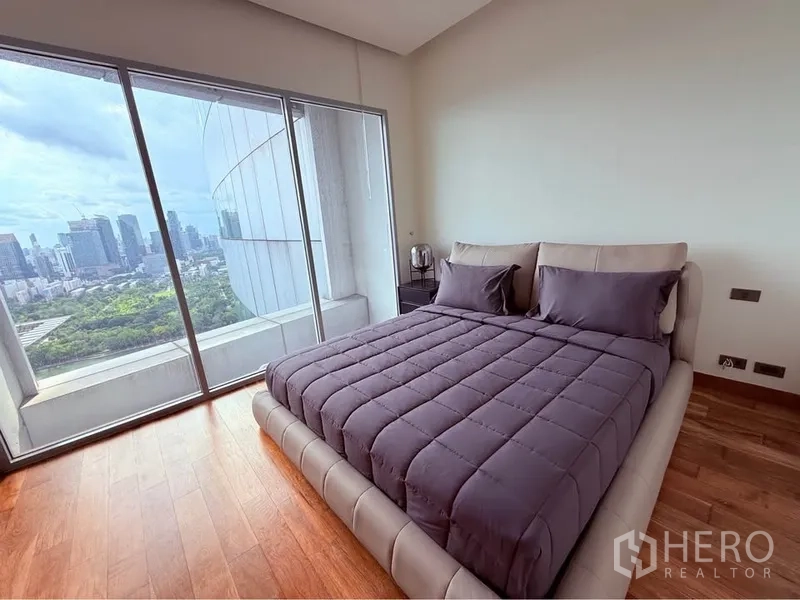 คอนโด ให้เช่าหรือขายในKhlong Toei, Bangkok - ห้องนอนเตียงผ้าสีเทา ประตูกระจกเต็มสูงออกสู่ระเบียง เห็นวิวเมืองและสวน