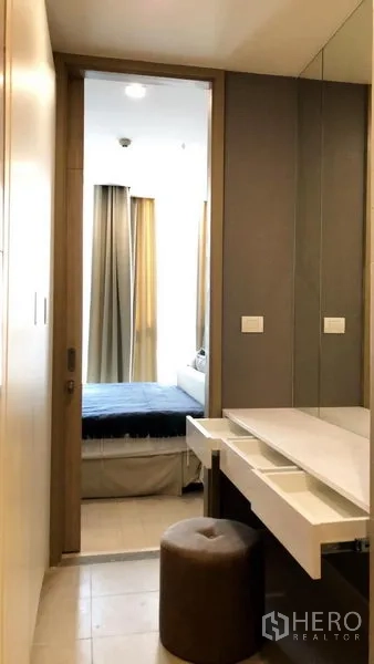 Condominium for rent in Pathum Wan, Bangkok - Dressing area with vanity and stool leading into a bright bedroom.