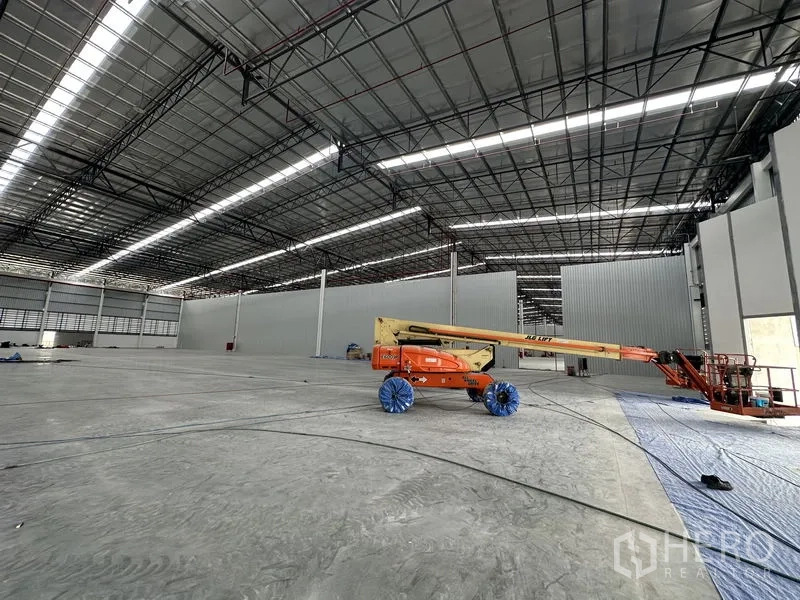 Factory for rent in Khlong Luang, Pathum Thani - Open manufacturing floor with boom lift under a high steel roof and skylight panels.