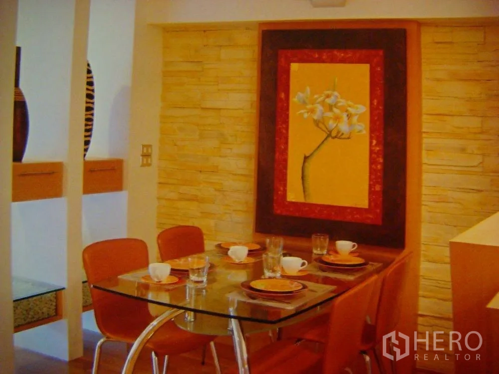คอนโด ให้เช่าในPathum Wan, Bangkok - มุมรับประทานอาหารโทนอุ่น โต๊ะกระจก เก้าอี้สีส้ม ผนังหินและภาพดอกไม้