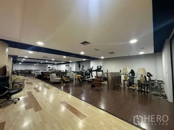 零售空间 出租 - 宽敞展厅，木地板、沙发区与健身器材，嵌灯明亮。