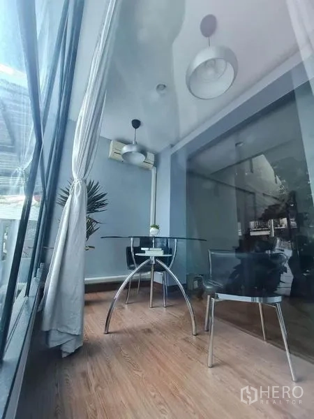 Townhouse for sale in Suan Luang, Bangkok - Bright glass sunroom dining area with round glass table, two chairs and pendant lights.