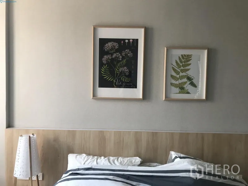 Condominium for rent in Watthana, Bangkok - Minimalist bedroom with light wood headboard and framed botanical artwork on soft gray walls.