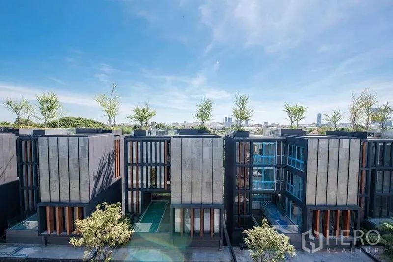 独立式住宅 出售在Prawet, Bangkok - 现代多层住宅外观，屋顶绿植与竖向立面，蓝天之下。