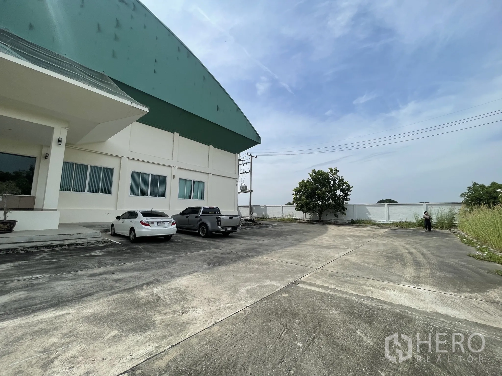 Warehouse for sale in Lat Lum Kaeo, Pathum Thani - Corner view showing the paved yard, boundary wall and parking area beside the warehouse.