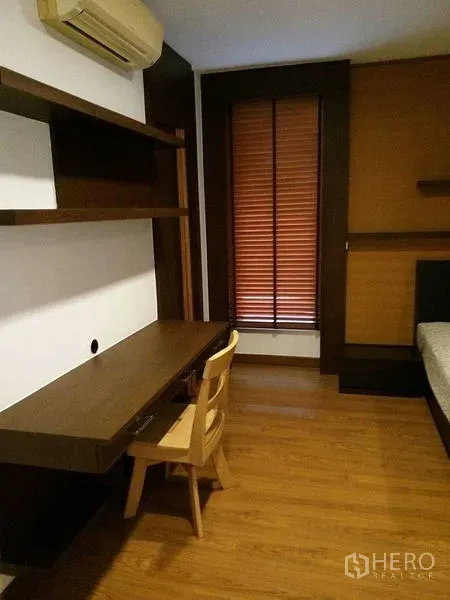 Condominium for rent in Sathon, Bangkok - Bedroom corner with built-in desk, wall shelving, wooden floor, and window with blinds.