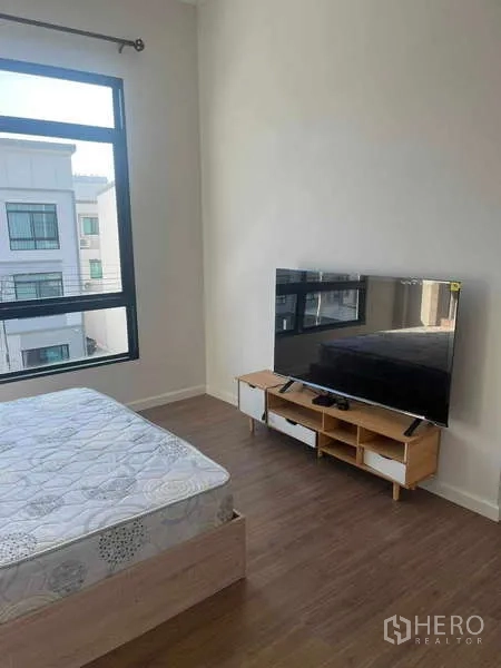 ทาวน์เฮาส์ ให้เช่าในSuan Luang, Bangkok - ห้องนอนสว่างพร้อมเตียง หน้าต่างบานใหญ่ พื้นไม้ และทีวีบนชั้นวางเตี้ย