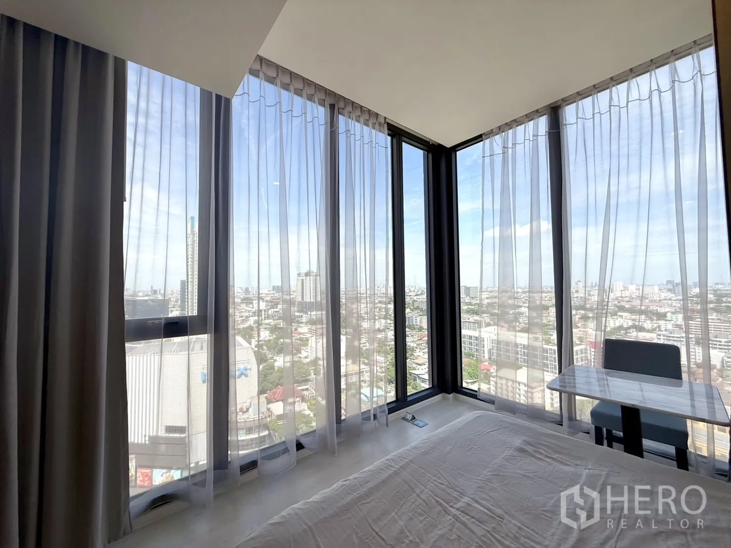 Condominium for sale in Chatuchak, Bangkok - Corner glazing with sheer curtains and a compact work desk by the window.