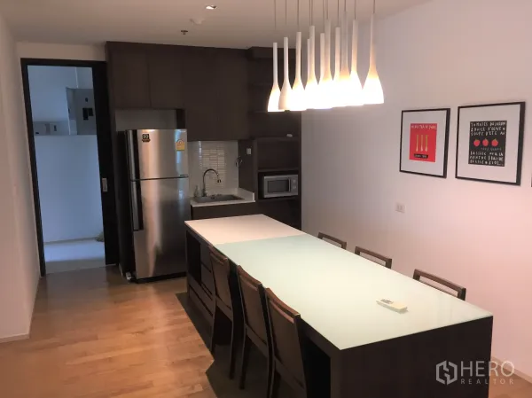 Condominium for rent in Watthana, Bangkok - Open kitchen and dining with long island table, pendant lights, stainless refrigerator and microwave.