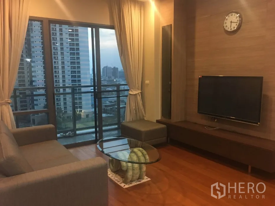 公寓 出租在Khlong Toei, Bangkok - 客厅配沙发与电视墙，落地窗通向城市景观阳台。