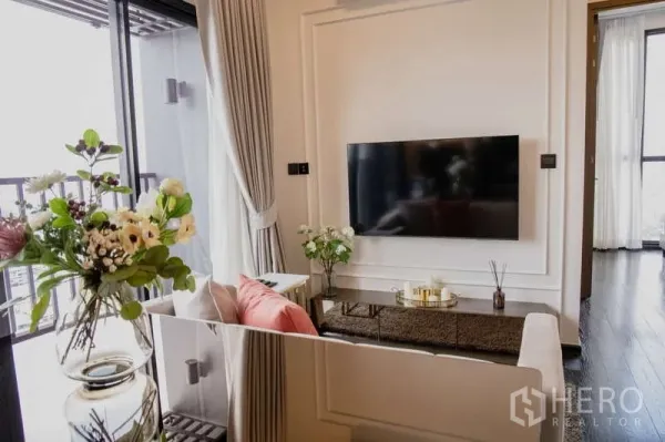 Condominium for rent in Watthana, Bangkok - Bright living room with wall-mounted TV, balcony access and floral decor.