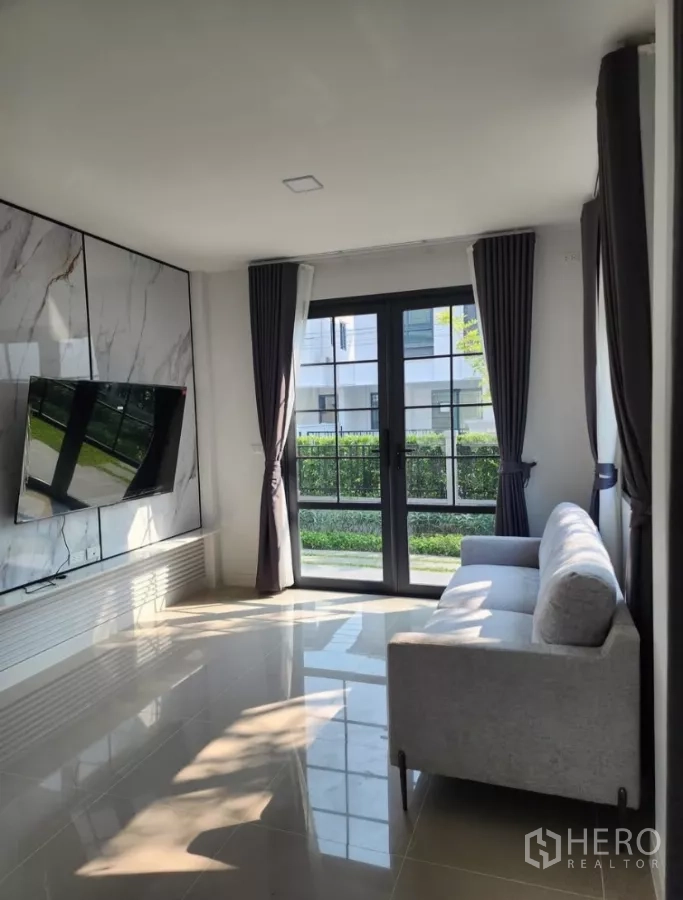 Detached House for rent in Bang Phli, Samut Prakan - Living room with marble TV wall, sofa and sliding doors to the garden