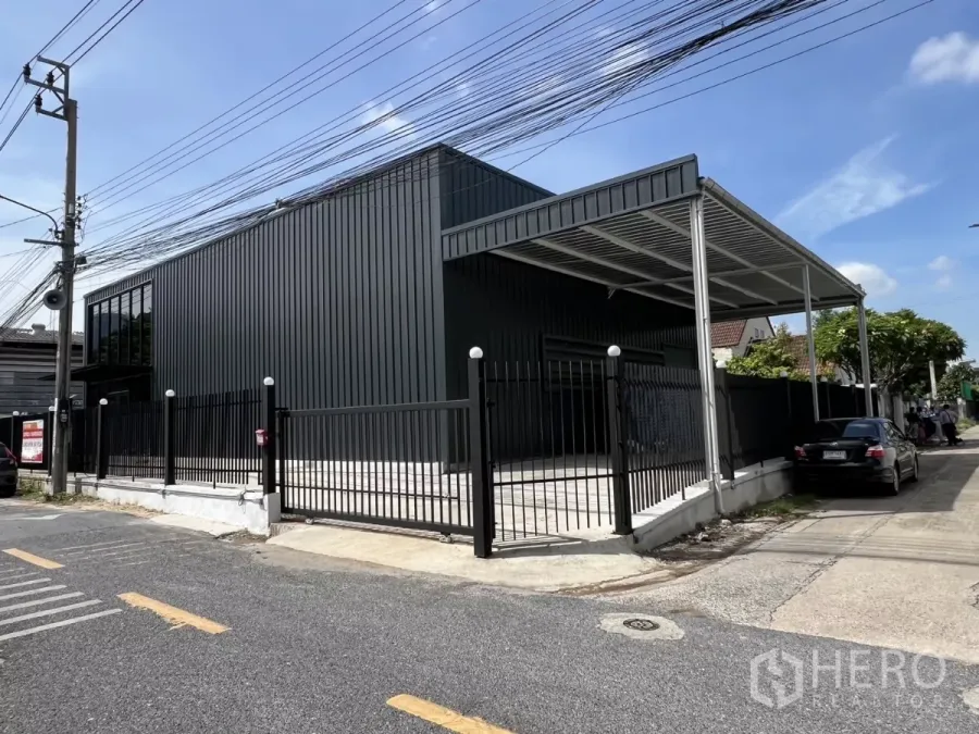 Warehouse for rent in Bang Na, Bangkok - Front elevation of the new warehouse showing sliding gate, canopy, and driveway parking.
