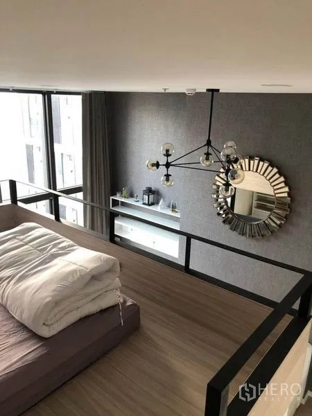 Condominium for sale in Ratchathewi, Bangkok - Mezzanine bedroom overlooking the living room with chandelier and decorative round mirror.
