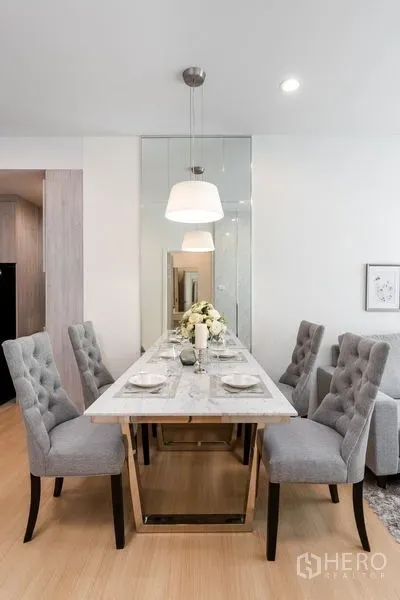 Condominium for sale in Yan Nawa, Bangkok - Dining space with four tufted chairs around a marble table beneath pendant lamps.