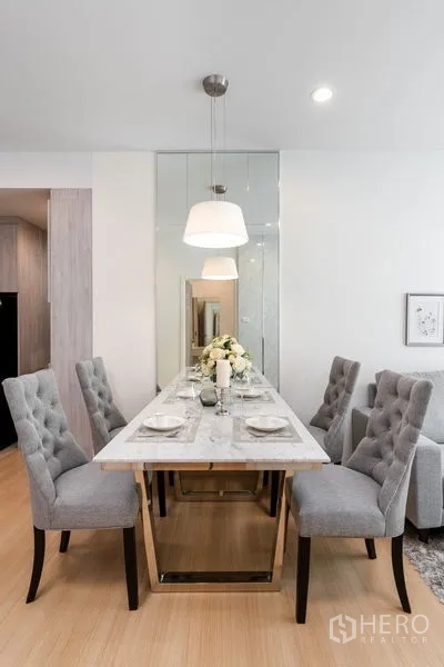 Condominium for sale in Yan Nawa, Bangkok - Dining space with four tufted chairs around a marble table beneath pendant lamps.