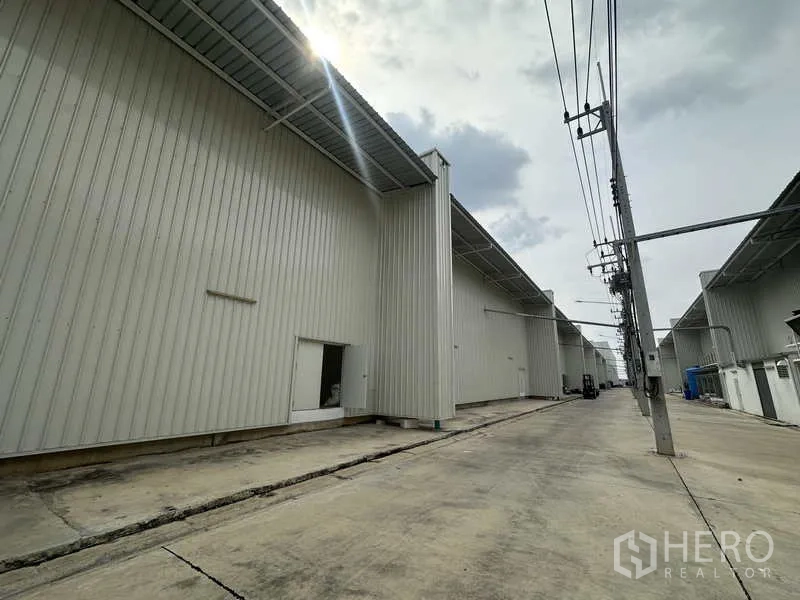 Factory for rent in Khlong Luang, Pathum Thani - Service lane behind factories with deep eaves and utility power poles.
