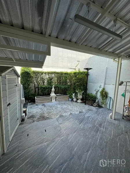 ทาวน์เฮาส์ ขายในLat Phrao, Bangkok - ลานเอนกประสงค์แบบมุงหลังคาปูหิน สีเทา มีพุ่มต้นไม้ ม้านั่ง และโรงเก็บของ