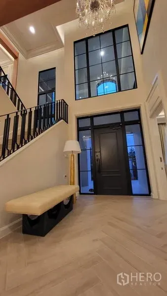 Detached House for rent or sale in Saphan Sung, Bangkok - Double-height foyer with black-framed glass door, chandelier, herringbone floor, and staircase.