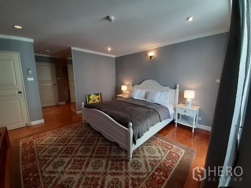 公寓 出租或出售在Watthana, Bangkok - 主卧配木地板与图案地毯，柔和灯光与灰色墙面。