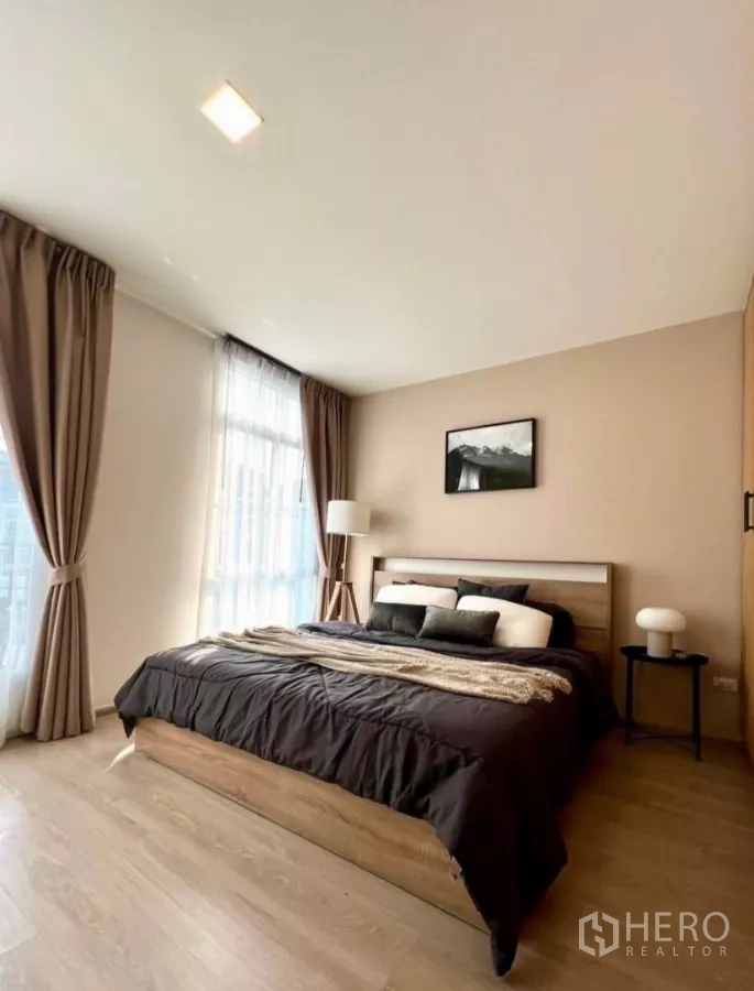 联排别墅 出租在Prawet, Bangkok - 通透明亮的主卧，大窗户与木质床架，配色柔和。