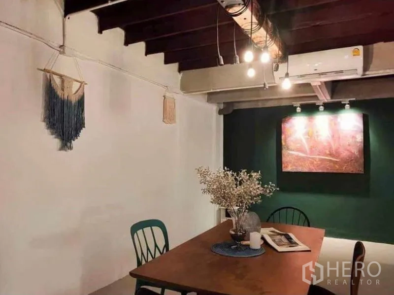 Detached House for rent in Pathum Wan, Bangkok - Dining space with hanging bulbs, air conditioner, dark green feature wall and framed artwork.