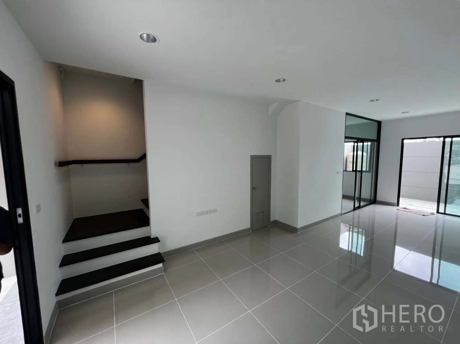 Townhouse for rent in Bang Khen, Bangkok - Open-plan living area with glossy tile floors, staircase, and sliding glass doors.