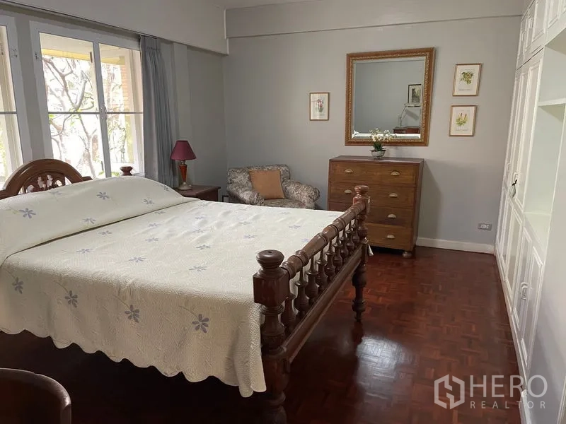 公寓 出租在Watthana, Bangkok - 卧室配经典木床架、五斗柜与休闲角落。