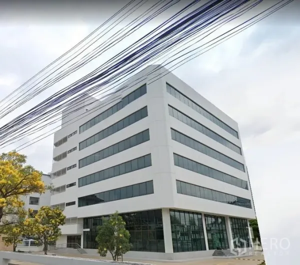 办公空间 出租在Din Daeng, Bangkok - 现代白色多层办公楼外观，横向窗带与转角玻璃首层，前有树木与铺装车道。