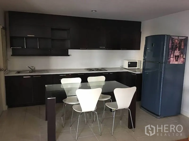 Condominium for rent or sale in Yan Nawa, Bangkok - Modern kitchen with dark cabinets, glass dining table, four white chairs, and a tall blue fridge.