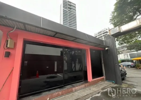 零售空间 出租在Watthana, Bangkok - 单层店面外立面，粉色框架配黑色大窗，远处高楼林立。