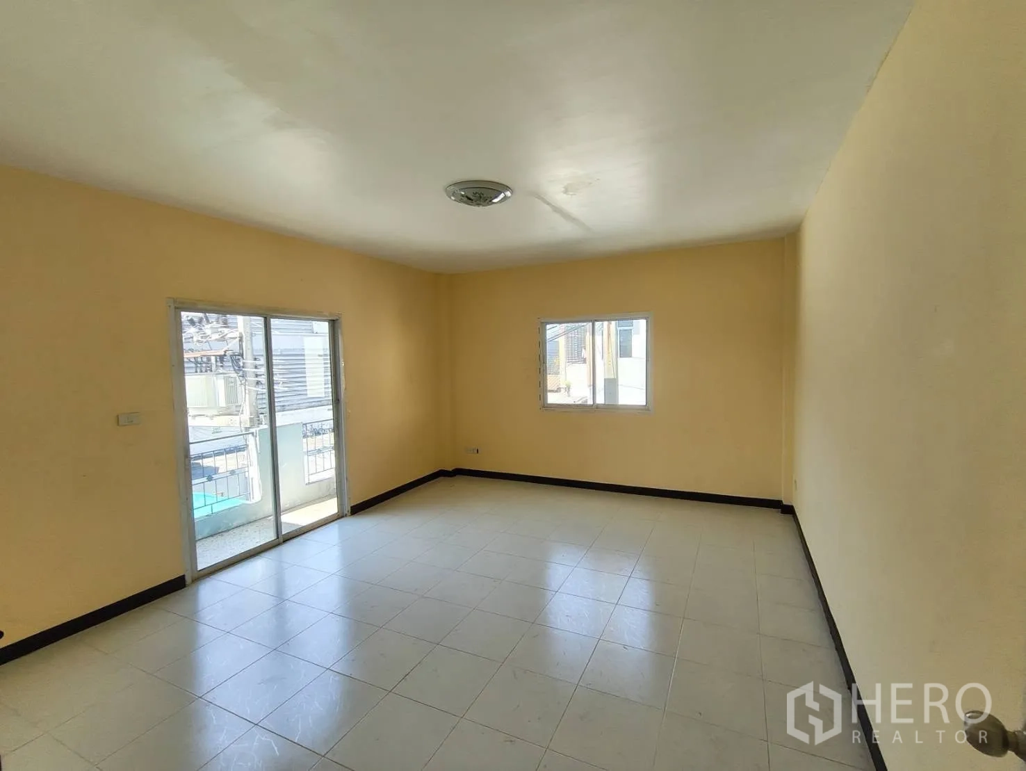 Factory for rent in Krathum Baen, Samut Sakhon - Bright empty room with tiled floor and a sliding glass door leading to a small balcony.