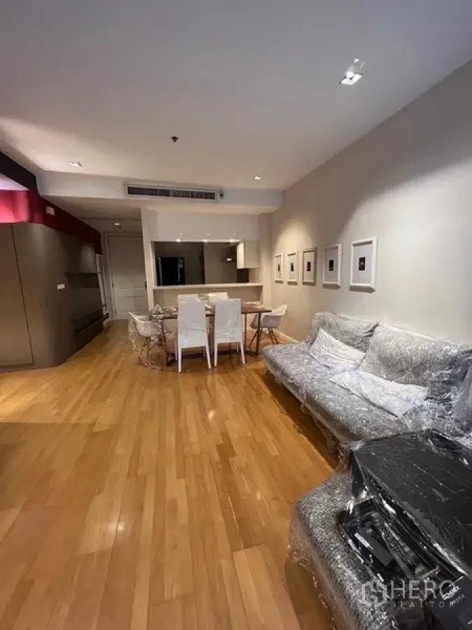 Condominium for rent in Pathum Wan, Bangkok - Open-plan living and dining area with wood flooring, framed art and a six-seat table.