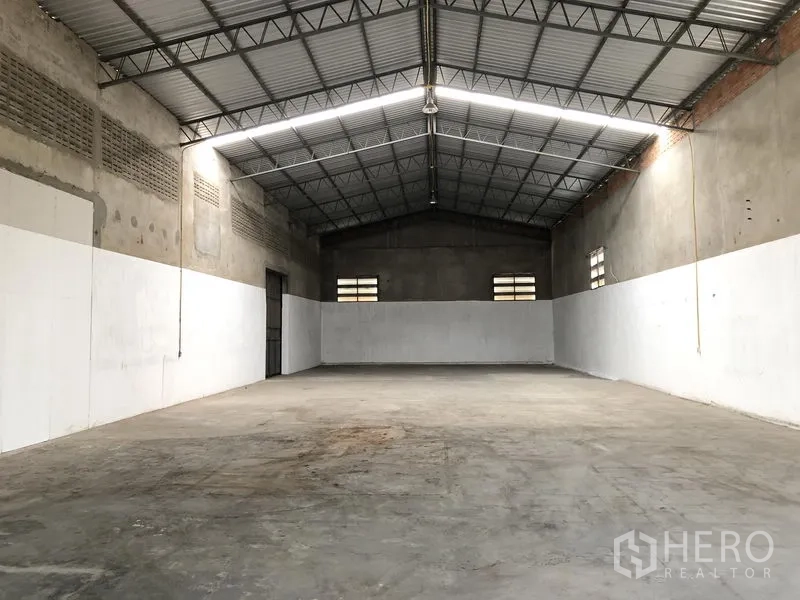Warehouse for rent in Mueang Pathum Thani, Pathum Thani - Spacious warehouse interior with high steel-truss roof, concrete floor, and ventilation windows.
