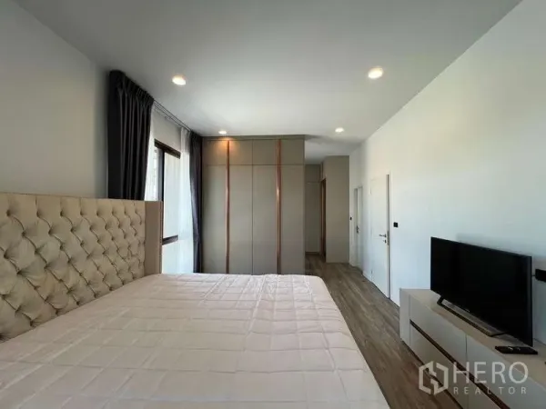 Detached House for rent in Bang Kapi, Bangkok - Bright master bedroom with upholstered headboard, built-in wardrobe and TV console.