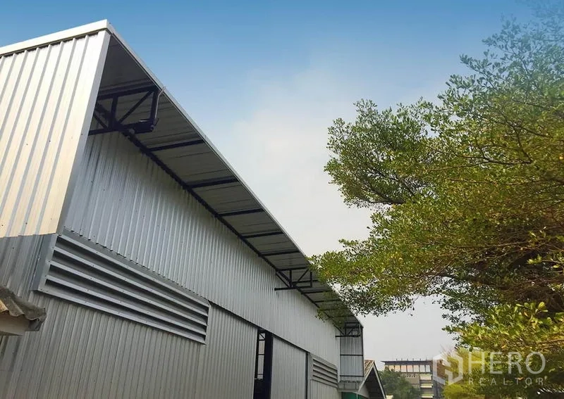 Warehouse for rent in Din Daeng, Bangkok - Metal-clad warehouse exterior with long eaves and tree-lined surroundings under a clear Bangkok sky.