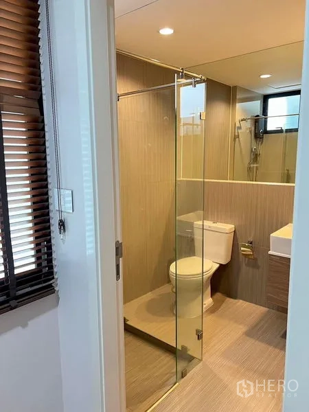 Townhouse for rent in Saphan Sung, Bangkok - Bathroom with glass shower enclosure, toilet and modern vanity beside window blinds.