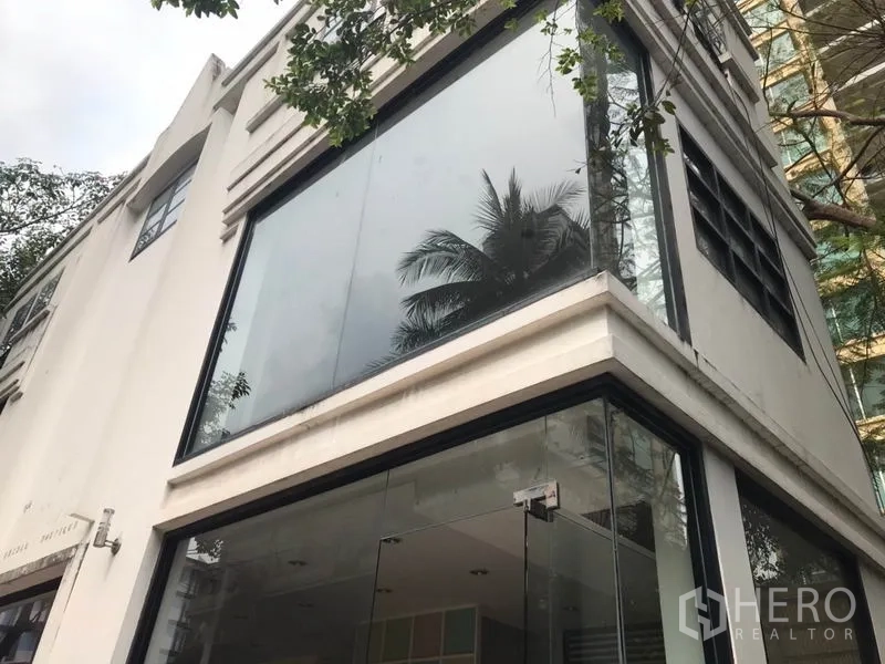 零售空间 出租在Watthana, Bangkok - 白色转角两层商铺外立面，整面玻璃窗映出树影