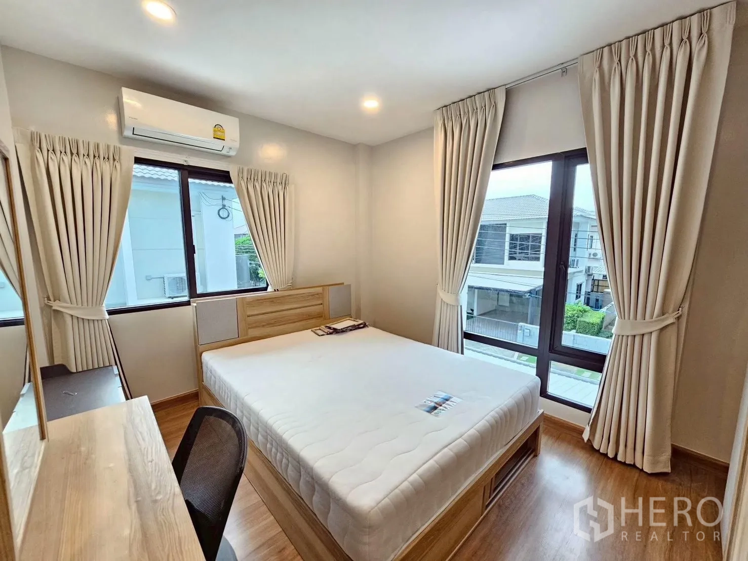 Detached House for sale in Bang Phli, Samut Prakan - Corner bedroom featuring a queen bed, big windows on two sides, light curtains, dressing desk, and wood flooring.