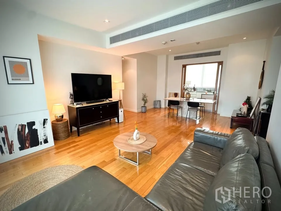 คอนโด for rent or sale in Khlong Toei, Bangkok - ห้องนั่งเล่นมีชั้นวางทีวี โต๊ะกลาง โซฟาหนัง และประตูบานเลื่อนไปยังห้องครัว